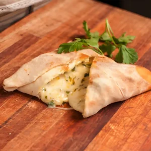 imagen de estilo de producto con una empanada armenia de queso y cebolla sobre tabla de cortar.